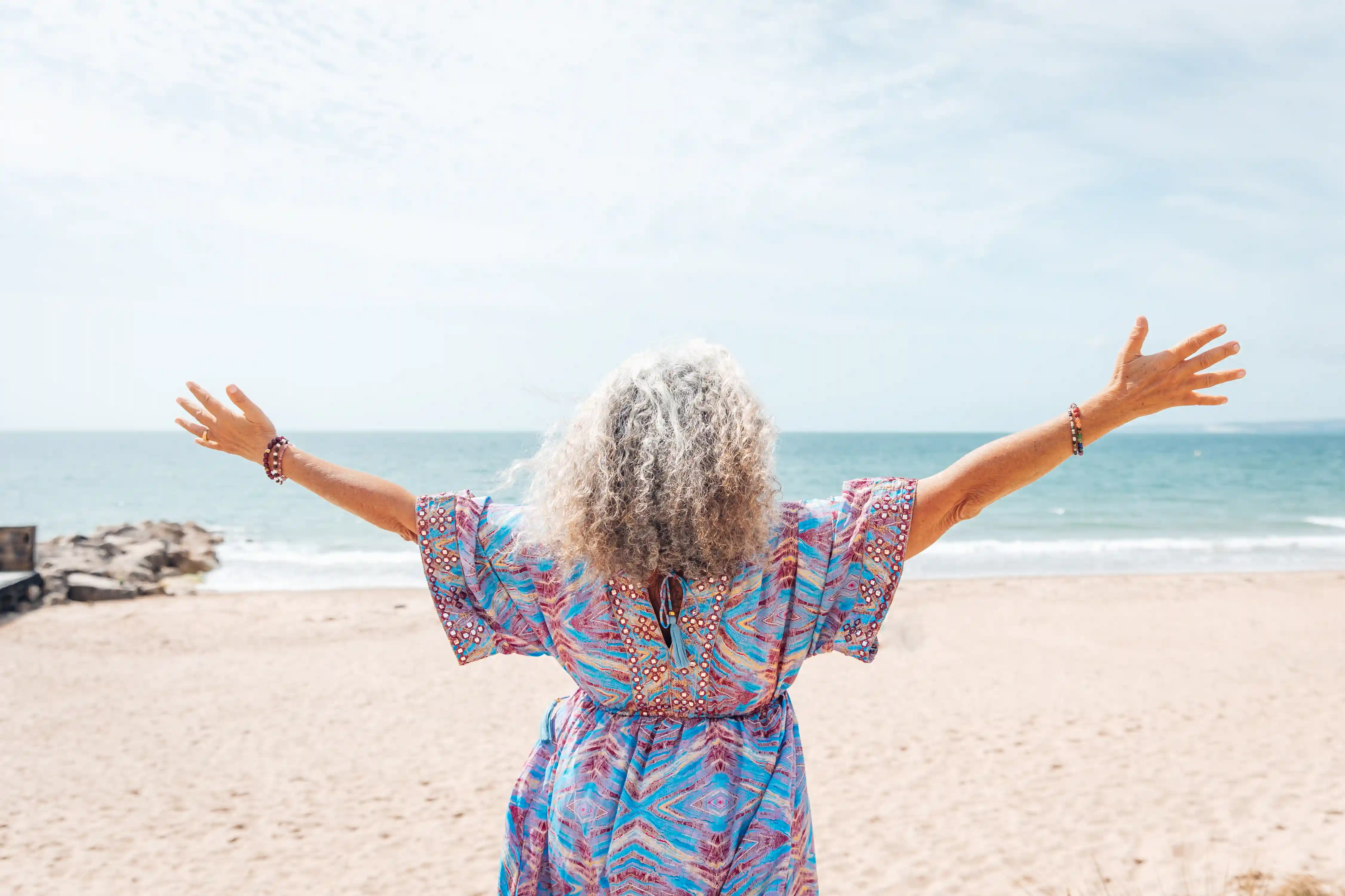 Jyoti with her arms open at the beach, looking out to sea.